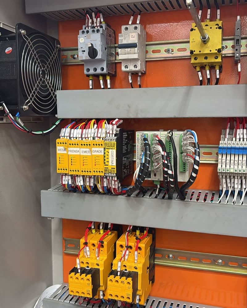 Quadro elétrico aberto com disjuntores-motor, relés de segurança amarelos, contatores e régua de bornes identificada